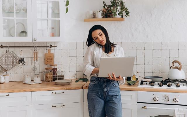 Vrouw in keuken op laptop en met gsm aan oor